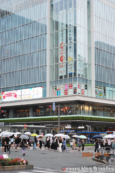 D60とAi NIKKOR 45mm f/2.8Pで一日一撮作例6、博多駅の交差点で傘をさして歩く人々。梅雨の真っ只中だ。