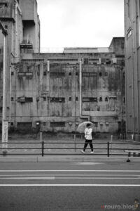 廃墟の壁の前を歩く通行人を撮影。Viltrox AF 50mm F2 AIR ＆ Nikon Zf で撮影。ピクチャーコントロールはモノクローム。