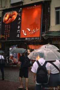 雨の日に唐揚げ屋さんの前を横切る人たちをViltrox AF 50mm F2 AIR ＆ Nikon Zf で撮影。ピクチャーコントロールはNeighborhood