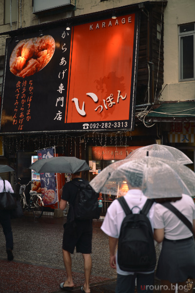 雨の日に唐揚げ屋さんの前を横切る人たちをViltrox AF 50mm F2 AIR & Nikon Zf で撮影。ピクチャーコントロールはNeighborhood