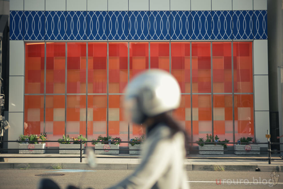 MR.DING Noxlux DG 50mm F1.2 とフレキシブルカラーの組み合わせ。不思議な模様の壁の前を走るバイク乗りの女性。