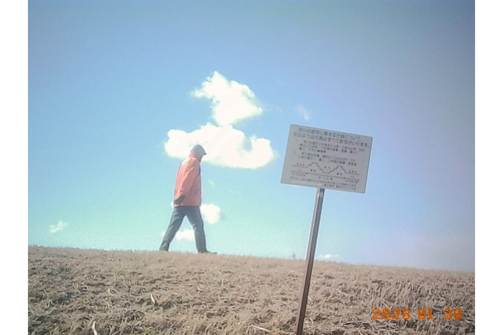 川辺を歩いてる人をKodak Charmeraで撮影。空の青とジャケットの赤のコントラストが良い。