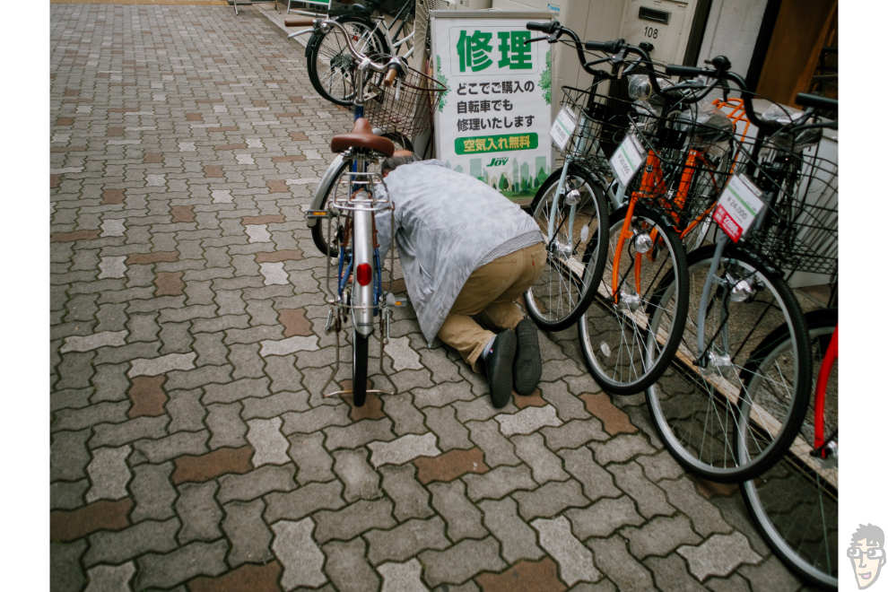 お爺さんが膝をついて自転車に空気を入れている。LUMIX GM5で撮影。