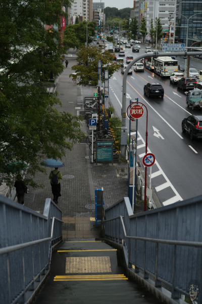 雨の日のズミクロンスナップ。歩道橋から歩道を眺める。通勤している人が歩いている。